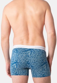 Boxer shorts bleus avec un motif floral, dotés d'une taille élastique blanche. Le matériau semble doux avec une coupe ajustée, mettant en valeur des motifs de feuillage en bleu plus clair.