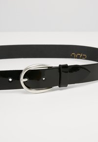 Zwarte gepatenteerde leren riem met een zilveren metalen gesp, een gladde textuur en een enkele pen met verschillende maatgaten.