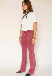 Jean évasé en velours côtelé rose avec poches avant et arrière, associé à un t-shirt blanc à col ras du cou et à un foulard noir imprimé autour du cou. Ballerines noires à bout pointu.