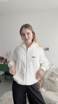 Felpa con cappuccio bianca con cerniera, realizzata in materiale a costine testurizzato e con tasca frontale, con un piccolo logo nero sul petto. Abbinata a pantaloni neri.