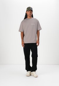 Camiseta gris de gran tamaño con el texto "no desperdicies la cultura", combinada con pantalones negros y zapatillas color off-white, complementada con una gorra de camuflaje.