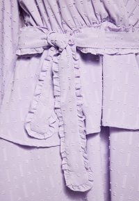 Rochie lavandă cu cordon din textură, având un margine volanată pe cordon și pe cusături, cu un model subtil pe întreaga suprafață.