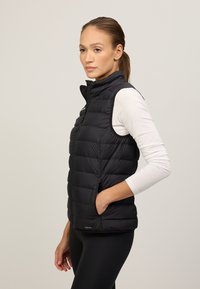 Schwarze ärmellose Steppweste mit horizontaler Steppung, Reißverschluss und seitlichen Taschen. Glattes Gewebe mit weichem Finish.