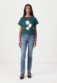 Mørkegrønn bomulls t-skjorte med korte ermer, med et lyst skjell- og solmotiv. Kombinert med lyseblå rettsnitt jeans.