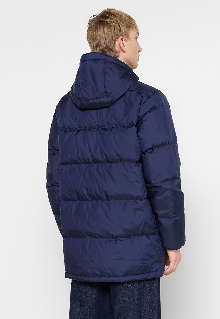 Doudoune bleu marine avec capuche, présentant un rembourrage cousu, une texture lisse et une coupe décontractée. Montre une vue arrière et des manches longues.