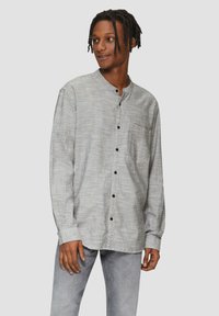 Langarmshirt in een grijs-witte ruitpatroon met een opstaand kraag, een borstzak en zwarte knoopsluitingen. Gecombineerd met lichtgrijze spijkerbroek.