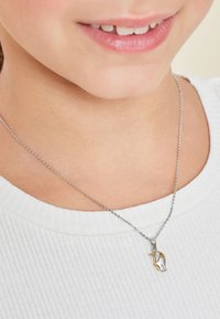 Sterling silverhalsband med en liten unicorn-hänge med guldkant, hängande på ett fint kedja. Bärs över en vit ribbad topp.