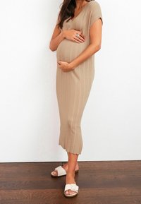 Robe beige en maille côtelée avec un col en V, des manches courtes et une silhouette ajustée. Associée à des sandales blanches glissantes. Design minimaliste.