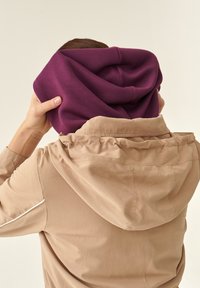 Il tessuto della felpa viola mostra una consistenza morbida, con una forma rilassata. La giacca beige presenta un cappuccio e dettagli di cucitura arricciata.