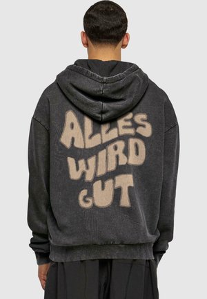 Sort hoodie med snor i hætten og stor beige skrift på ryggen, der står "ALLES WIRD GUT." Blødt, struktureret stof.