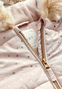 Chaquetón de plumas rosa claro con un patrón metálico de estrellas en oro rosado, cuello de felpa y detalles de cremallera dorados. La tela parece suave y lisa.