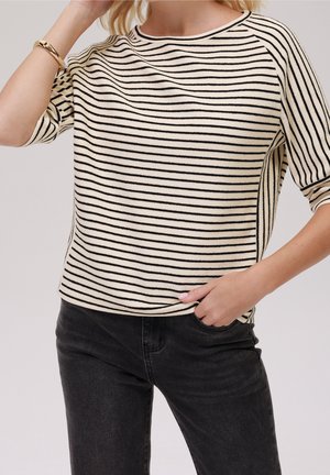 Striped sweater in cream and black, featuring a round neckline, short sleeves, and a relaxed fit. Textured fabric. Paired with dark jeans.