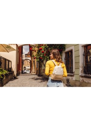 Light beige backpack with a smooth texture, dual shoulder straps, and a front zipper pocket, worn over a bright yellow long-sleeve shirt.