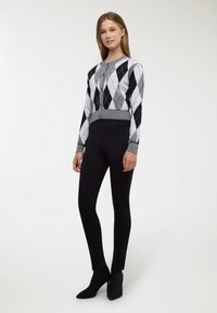 Cardigan a motivo rombi in bianco e nero, design corto, polsini grigi, chiusura con bottoni, abbinato a pantaloni neri aderenti e décolleté nere a punta.