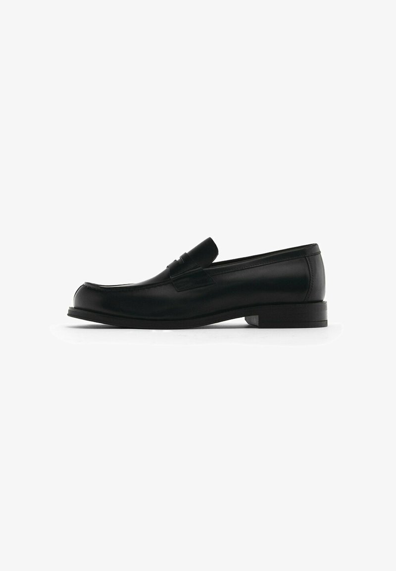 Black leather loafers with a rounded toe, featuring a decorative front tassel, flat heel, and subtle stitching details along the edges.