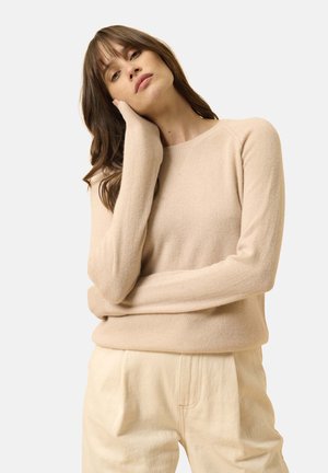 Beżowy sweter z wełny z okrągłym dekoltem, długimi rękawami i luźnym krojem, w połączeniu z jasnymi, teksturowanymi spodniami. Miękki, minimalistyczny design.