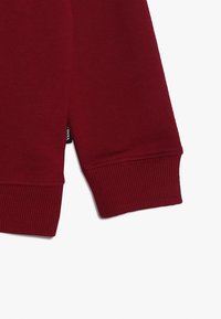 Felpa bordeaux con maniche che presentano un polsino a coste, tessuto morbido e un piccolo etichetta nera con testo bianco sul lato della cucitura.