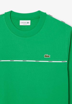 Green cotton t-shirt featuring a crew neck, white accent stripe with "LACOSTE," and a crocodile logo on the left chest. Classic fit design.