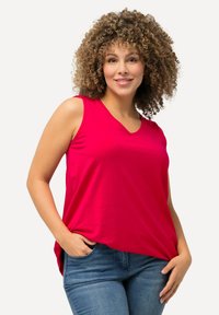 Mouwloze v-hals top van felroze stof, met een losse pasvorm en een ronde zoom. Gecombineerd met mid-rise blauwe jeans.