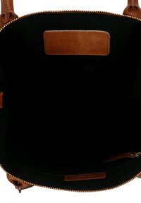 Vista interior de un bolso de mano abierto de cuero marrón que muestra el forro de tela negra, un bolsillo con cremallera y una etiqueta de cuero cosida con la marca.