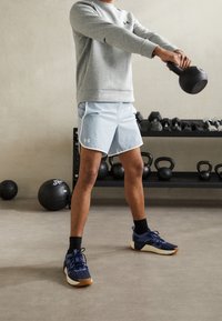 Gray sweatshirt, light blue shorts with white trim, and dark sneakers with textured design. Held kettlebell in a gym setting.