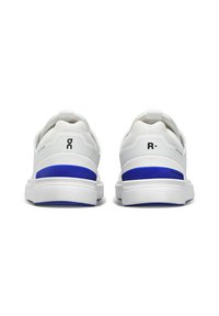Zapatillas deportivas blancas con una parte superior texturizada, acentos azules en el talón y una suela acolchada, con tirantes para facilitar su uso.