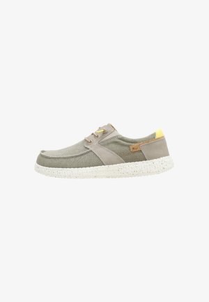 Zapatilla casual de lona gris con suela blanca moteada, detalles beige y pequeño detalle amarillo en el talón, vista lateral.