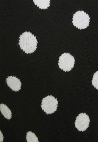 Black fabric featuring white polka dots in varying sizes, with a soft texture and ribbed knit pattern. Dots are evenly spaced throughout.