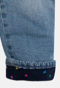 Džíny z denimu s světle modrým omakem, s ohrnutým lemem, který odhaluje námořnickou modrou fleecovou podšívku zdobenou barevnými puntíky.