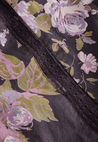 Tissu foncé avec imprimé floral rose et vert, avec une bande verticale de dentelle foncée traversant le centre.