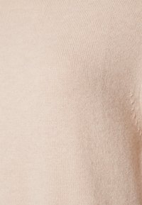 Tessuto di maglione beige a maglia, texture liscia, dettagli di coste fini, colore chiaro con sottili variazioni, senza schemi o accenti distintivi visibili.