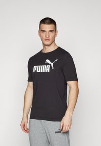 Melnas īsām piedurknēm t-krekls ar lielu baltu Puma logotipu priekšā, izgatavots no mīksta auduma ar apaļu kakla izgriezumu.