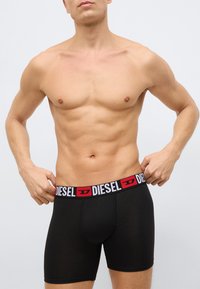 Czarne bokserki o dopasowanym kroju, z kontrastującym białym i czerwonym paskiem w talii z logo "DIESEL". Gładka faktura materiału.