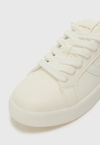 Sneaker in pelle bianca con punta arrotondata, superficie testurizzata e lacci bianchi piatti. Presenta cuciture sottili e un dettaglio con logo vicino alla linguetta.