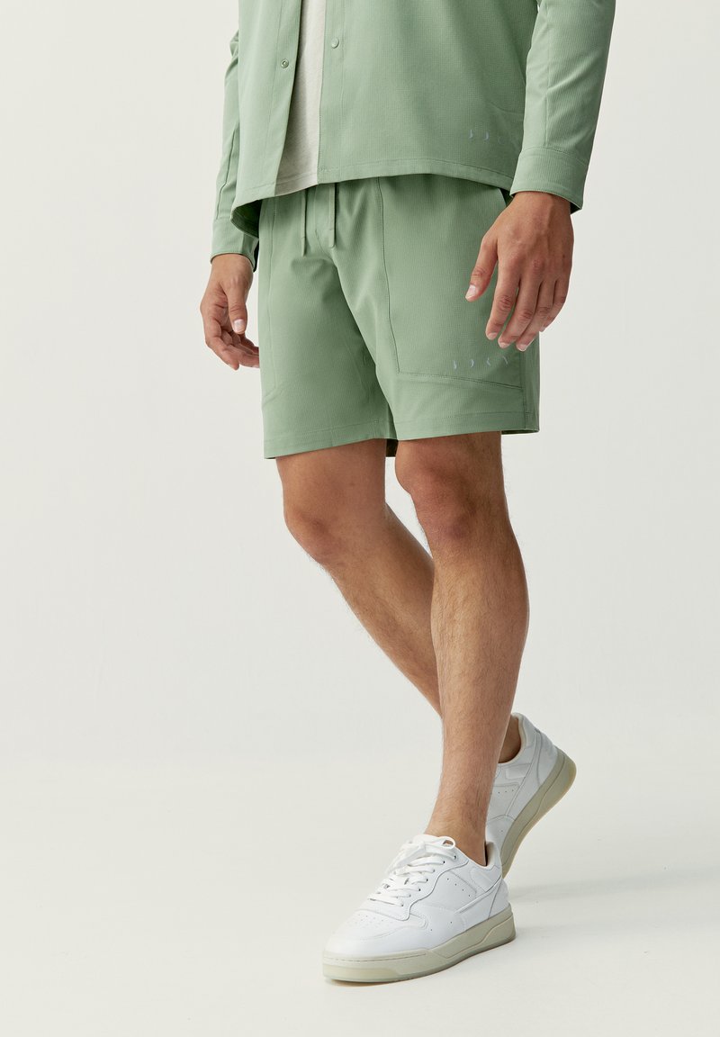 Mynta gröna shorts med avslappnad passform, med en elastisk midja och diskreta logodetaljer, kombinerade med vita sneakers.