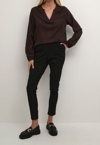 Brun satinbluse med V-hals, der har lange ærmer. Sammen med skræddersyede sorte bukser og sorte loafers med guldhardware detaljer.