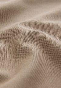 Jasnobeżowy teksturowany materiał z delikatnym wzorem w kratkę, z widocznymi miękkimi fałdami i gładką powierzchnią. Grube włókna są widoczne w całej powierzchni.