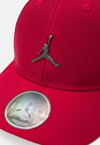 Rote Mütze aus strukturiertem Stoff, mit einem silbernen Jumpman-Logo und einem runden Etikett mit einem Verlaufsdesign.