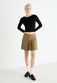 Un haut à manches longues noir associé à une jupe plissée marron, avec une texture lisse, taille haute et des chaussures plates classiques avec des chaussettes blanches.