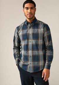 Camisa de cuadros navy con cuello abotonado, que presenta rayas en azul, marrón y crema. Fabricada con una tela suave y con un detalle de bolsillo en el pecho.