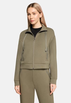 Olivengrøn cropped lynlåsjakke med teksturerede detaljer og snørejustering. Blødt materiale, sidelommer med nittepynt.