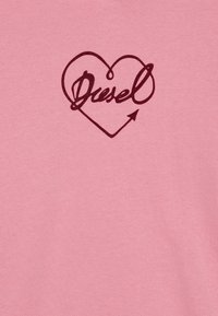 T-shirt di cotone rosa con un design a cuore rosso scuro che integra la parola "Diesel" nella forma e un accento a freccia.