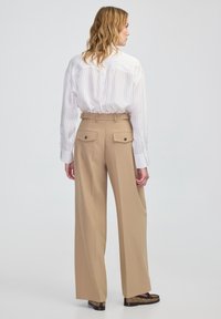 Beige wijde broek met een hoge taille, twee achterzakken en een zachte textuur, gecombineerd met een wit gestreept shirt met lange mouwen.