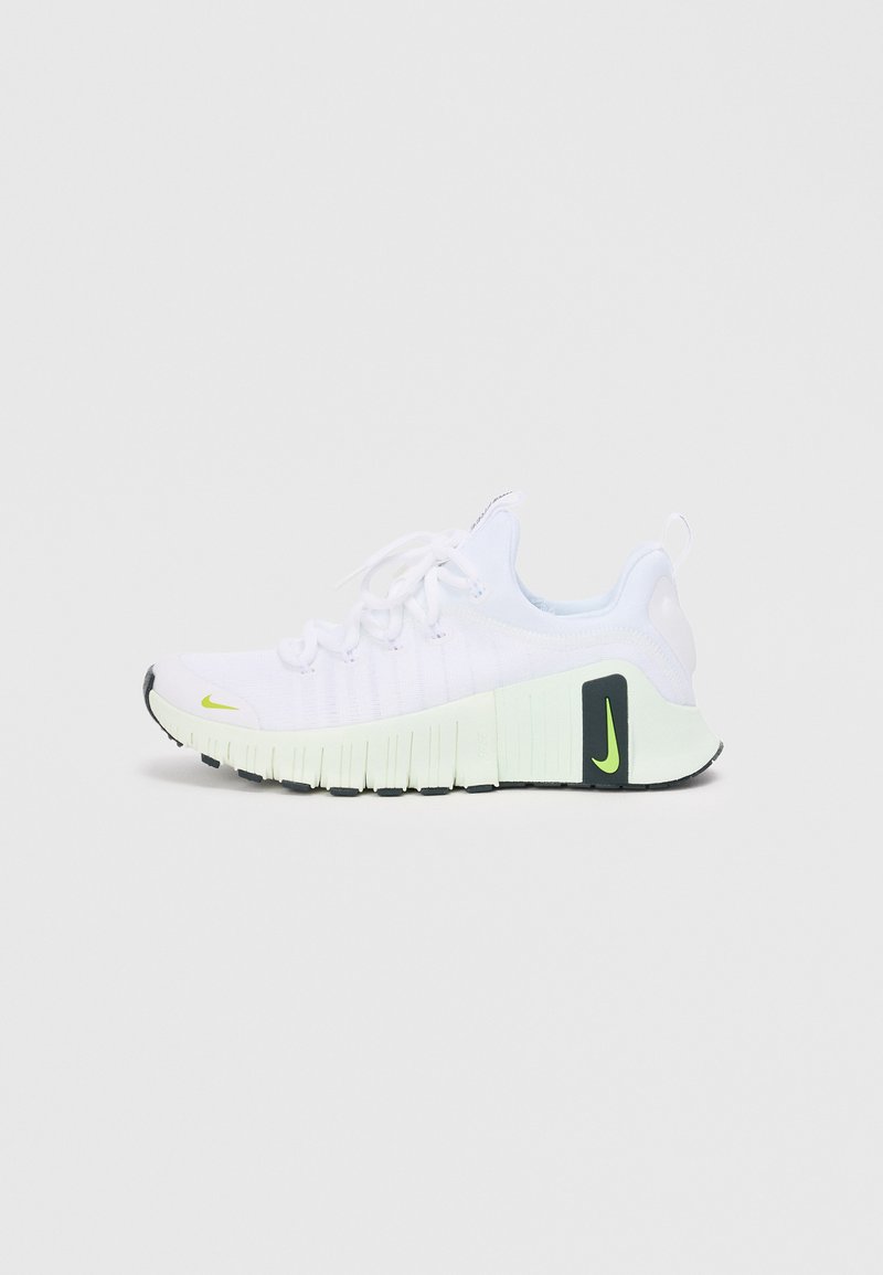White athletic shoes with textured fabric upper, neon yellow accents, and a thick black and green sole. Features lace-up design and rear pull tab.
