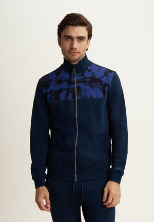Giacca zip-up blu navy con design a camo blu sulla parte frontale superiore, tessuto morbido, colletto alzato e polsini a coste.