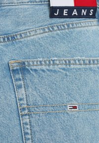 Vaqueros de denim azul claro con una etiqueta marino que lleva el texto "JEANS" y un pequeño acento de logo con franjas rojas, blancas y azules cerca de la costura del bolsillo.