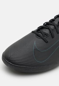 Chaussure de sport Nike noire avec un dessus texturé à motif en chevron, un nez renforcé et un logo swoosh bien visible dans une teinte plus sombre.