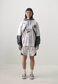 White athletic outfit with gray accents, featuring signature prints. Includes a hooded top and matching shorts, paired with sneakers.