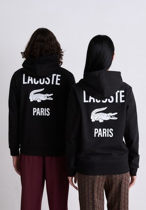 Black hoodies with white "LACOSTE" and "PARIS" text, featuring a crocodile graphic on the back. Soft fabric, relaxed fit, and standard cuffs.