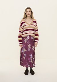 Gestreifter Strickpullover in Cremetönen, Rot und Pink. Floraler Maxirock in tiefem Burgunderrot mit blauen und goldenen Akzenten. Dunkles Schuhwerk rundet das Outfit ab.
